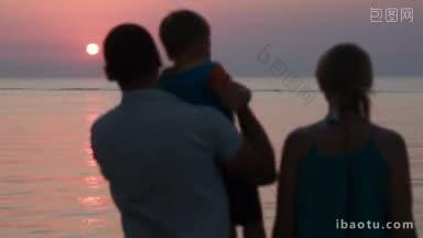 父亲抱着儿子，他们拥抱着母亲，在海上观看美丽的日落